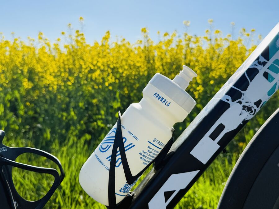 GRØNBLÅ komposterbar cykelflaske i flaskeholder med en gul rapsmark i baggrunden